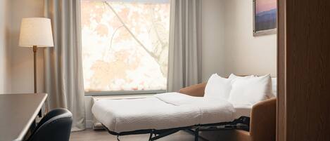 A hotel room with a bed, a desk, a chair, and a window with curtains.