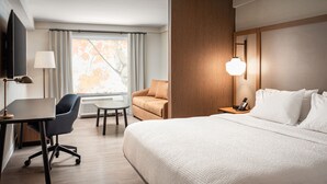 Ein Hotelzimmer mit einem großen Bett, einem Schreibtisch mit Stuhl, einer Couch, einem Fernseher und einem Fenster mit Vorhängen.