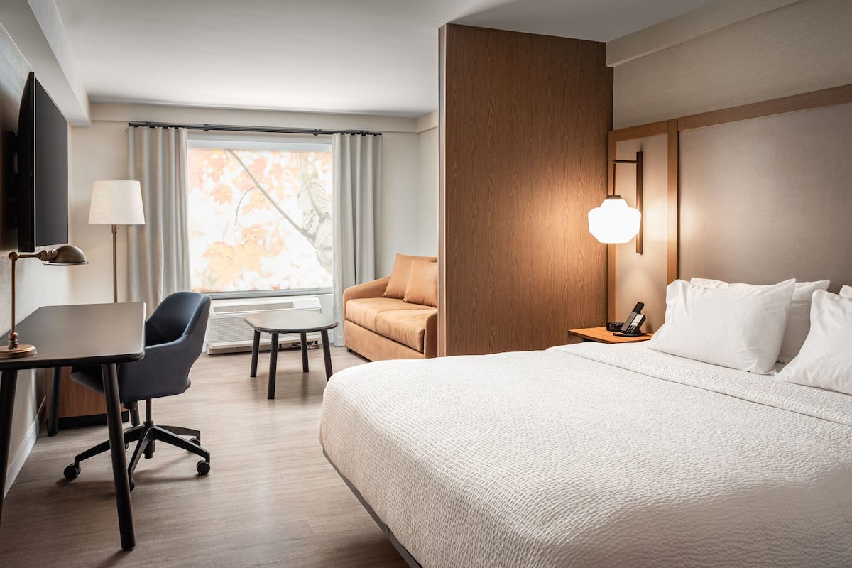 A hotel room with a large bed, a desk with a chair, a sofa, a TV, and a window with curtains.