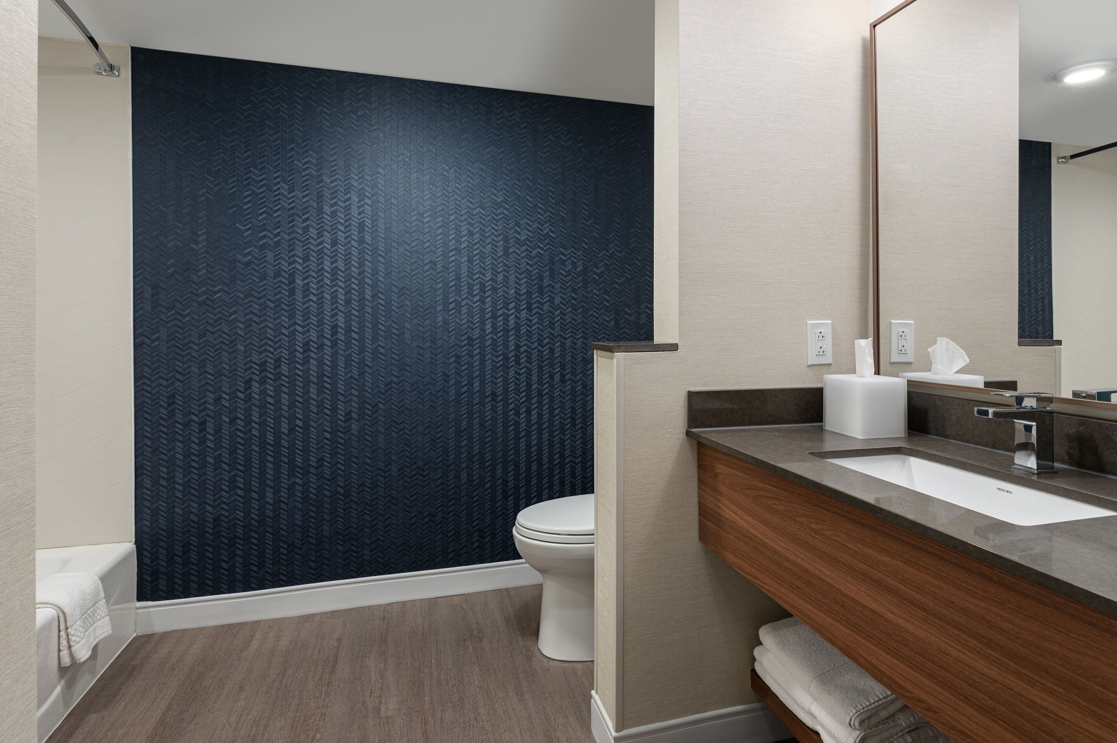 A modern bathroom with a dark patterned wall, a white toilet, a wooden vanity with a sink, and a mirror.