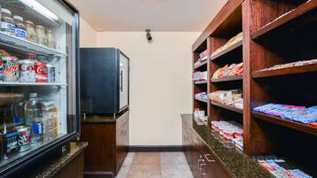 A kitchenette with a refrigerator stocked with beverages, a microwave, and shelves with snacks and toiletries.