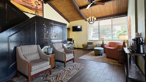 A spacious living room with a high ceiling, a large window with blinds, a fireplace, and a coffee table.