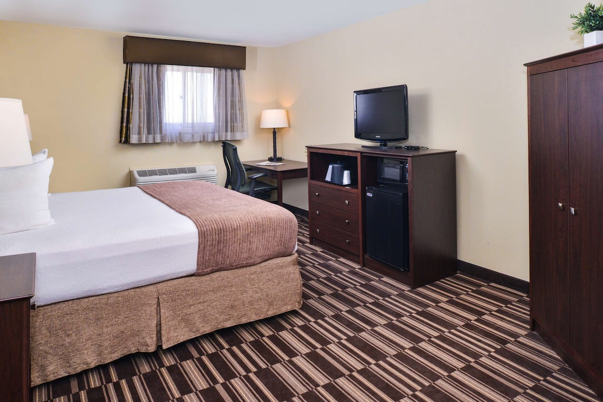A hotel room with a large bed, a desk with a computer, a television, and a wardrobe.