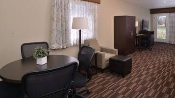 A hotel room with a round table, two chairs, a sofa, a cabinet, a TV, and a lamp.