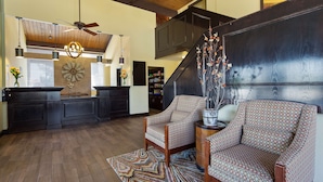 A spacious living area with a high ceiling, wooden beams, a modern kitchen, and a staircase leading to an upper level.