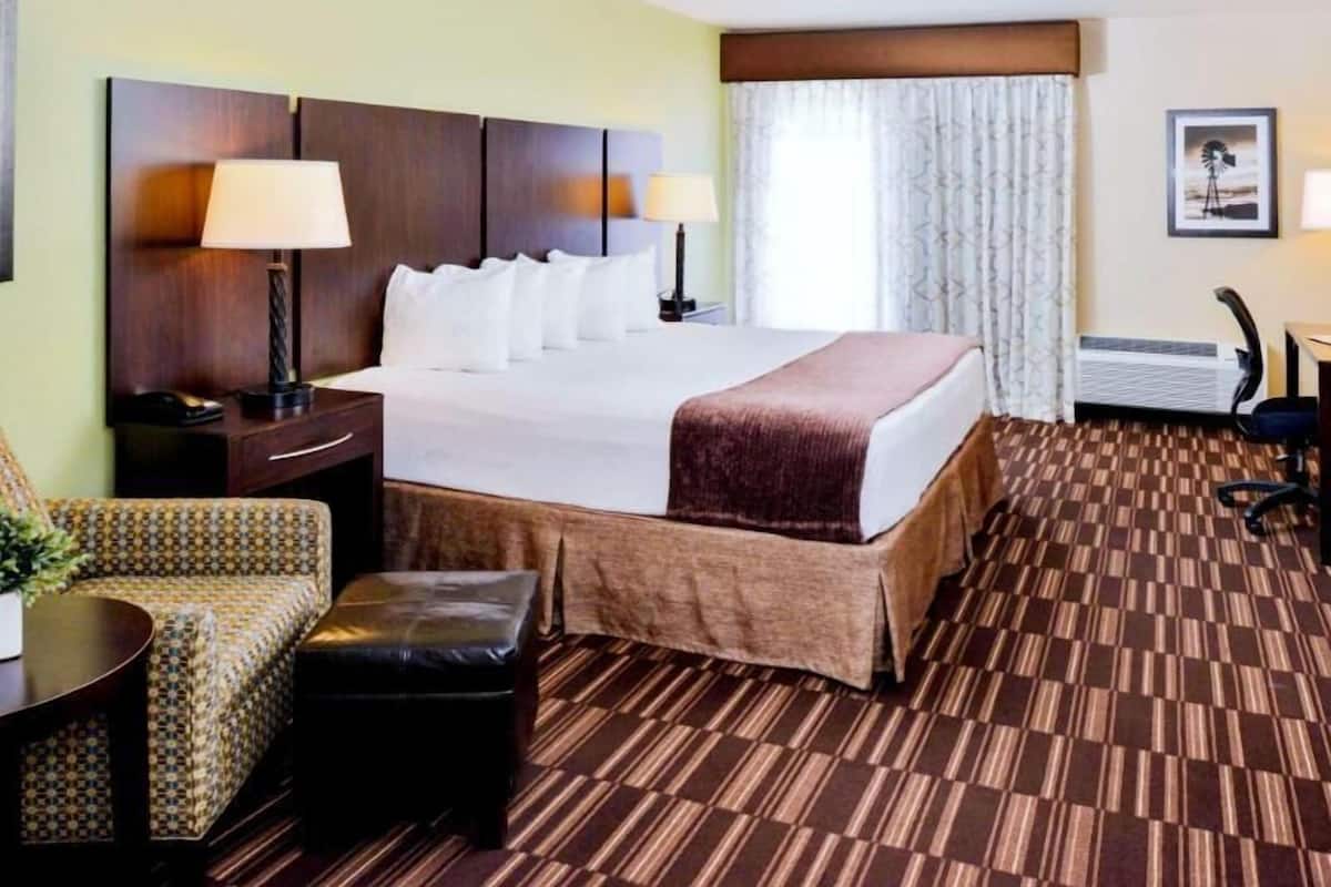 A hotel room with a large bed, two bedside tables, a chair, a small table, and a window with curtains.