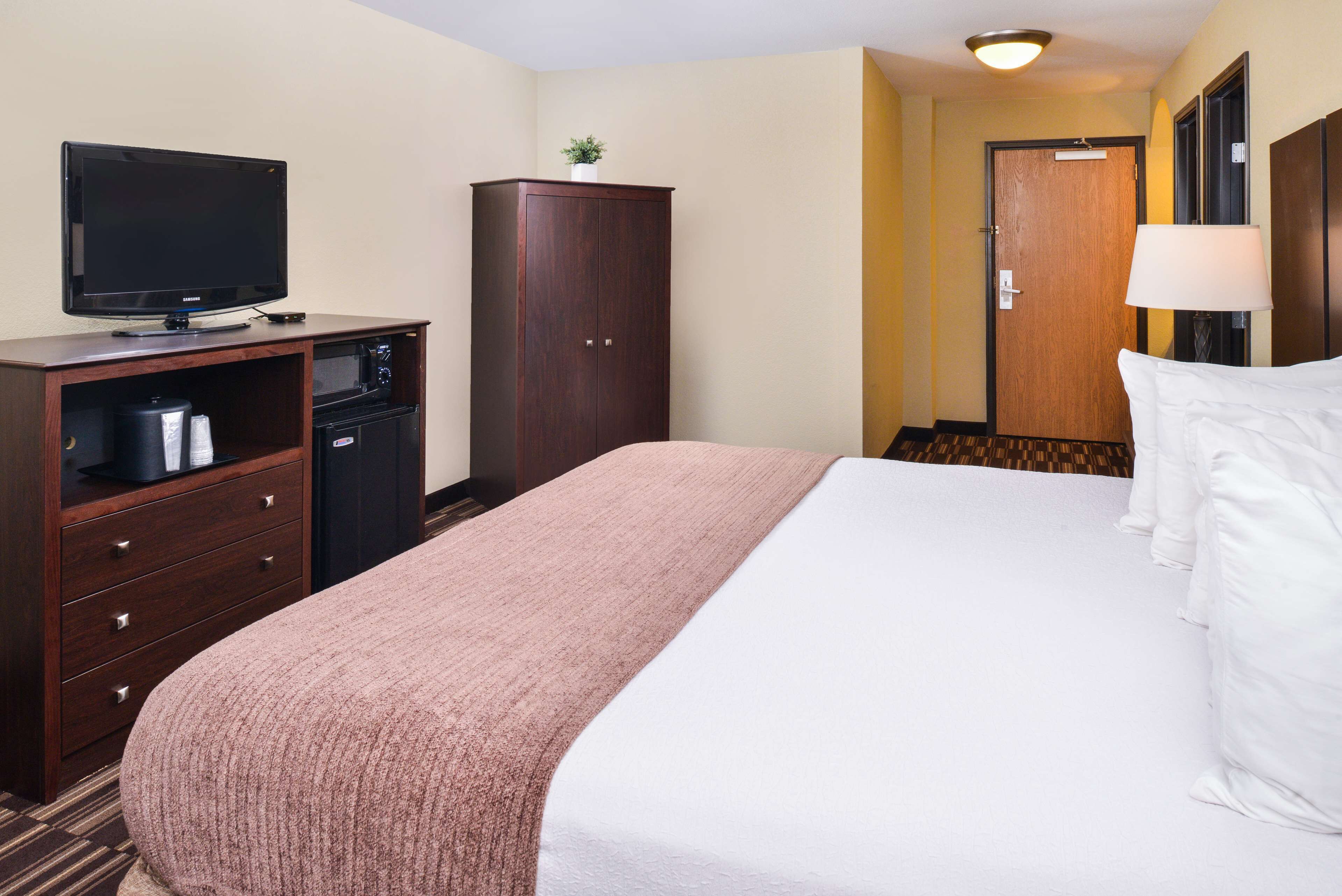 A hotel room with a bed, a television, a minibar, and a wardrobe.
