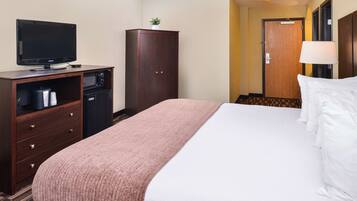 A hotel room with a bed, a television, a minibar, and a wardrobe.