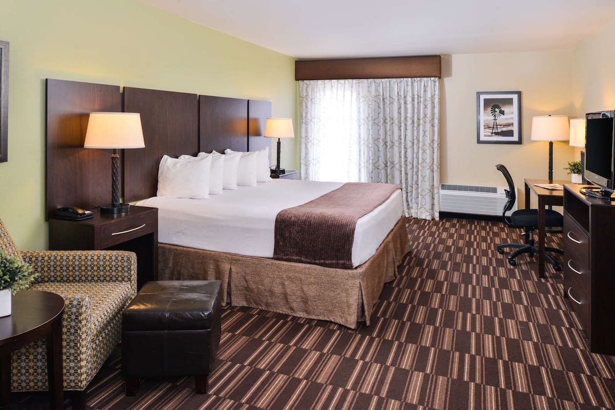 A hotel room with a large bed, two bedside tables with lamps, a desk with a chair, a television, and a window with curtains.