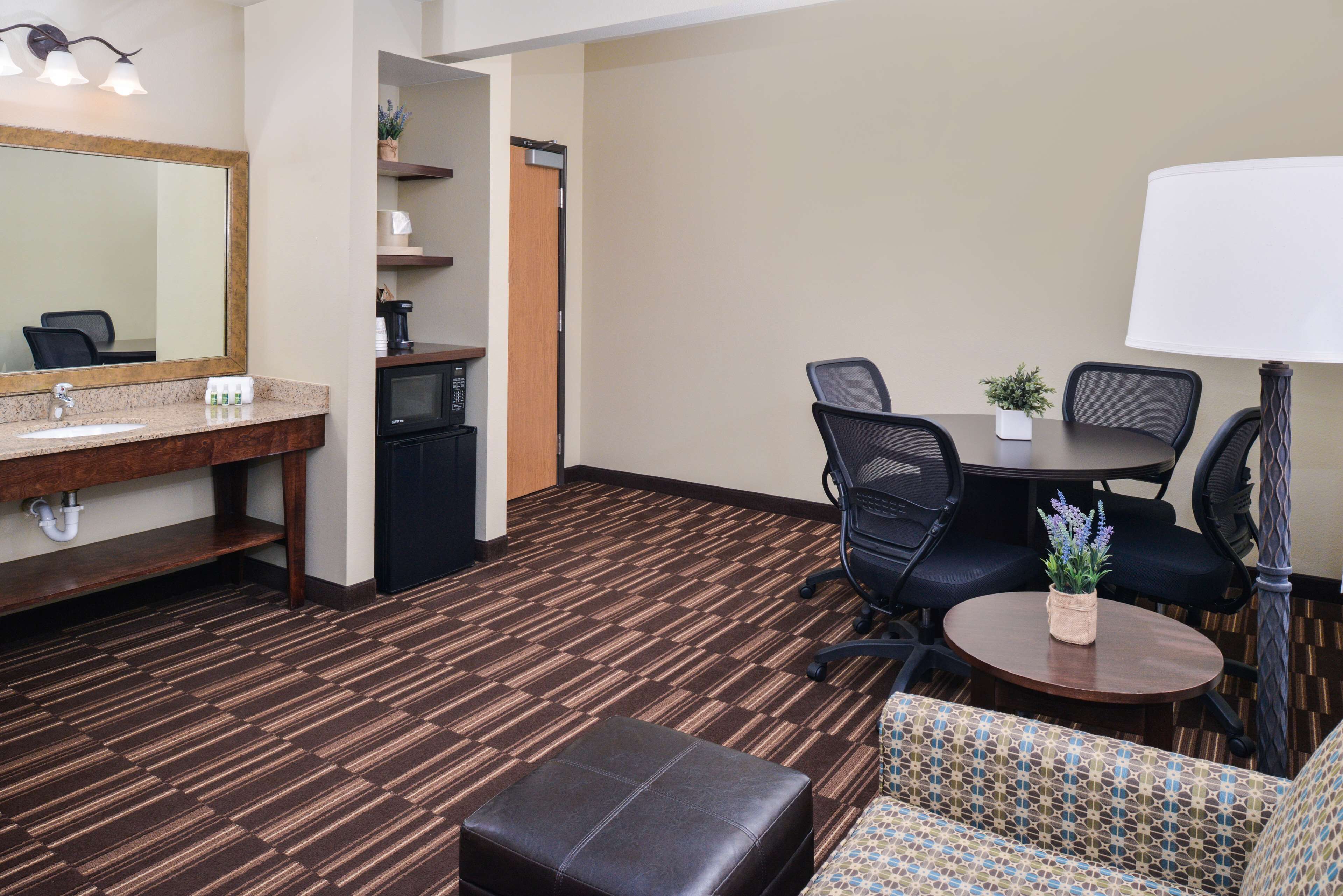 A hotel room with a kitchenette, a dining area with a table and chairs, a sofa, and a lamp.