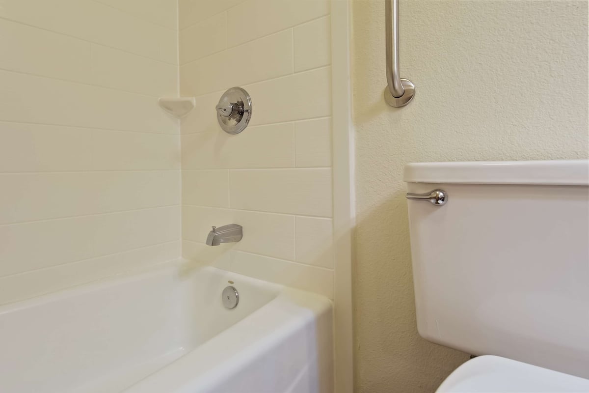 A bathroom with a white bathtub, a toilet, and a grab bar on the wall.