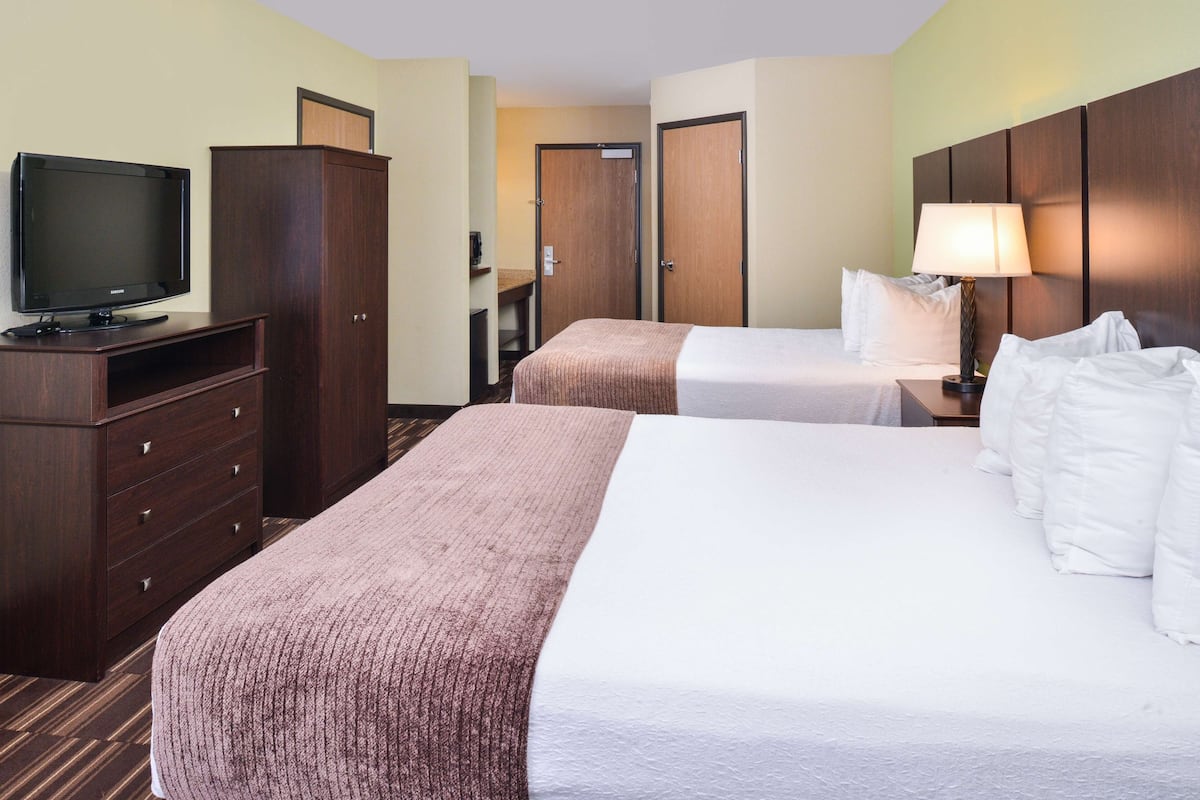 A hotel room with a large bed, a smaller bed, a TV on a dresser, and a desk with a lamp.
