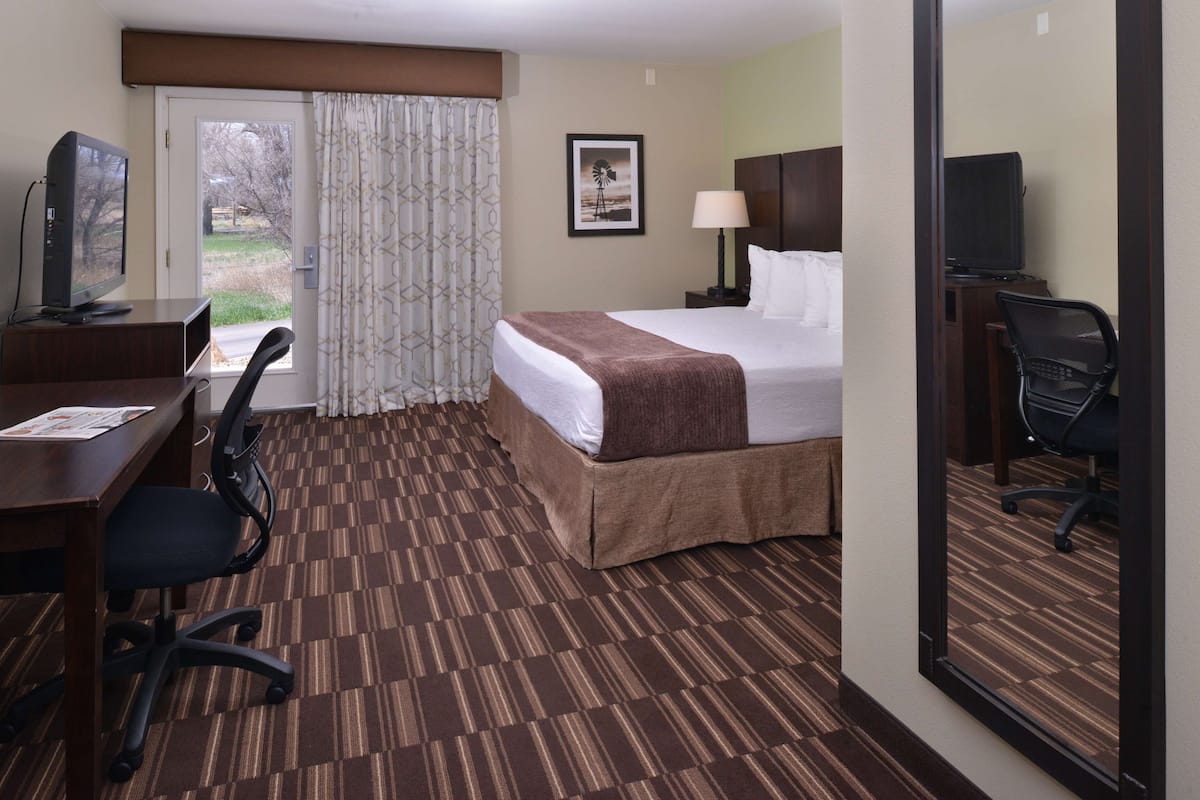 A hotel room with a bed, desk, chair, television, and a window with curtains.