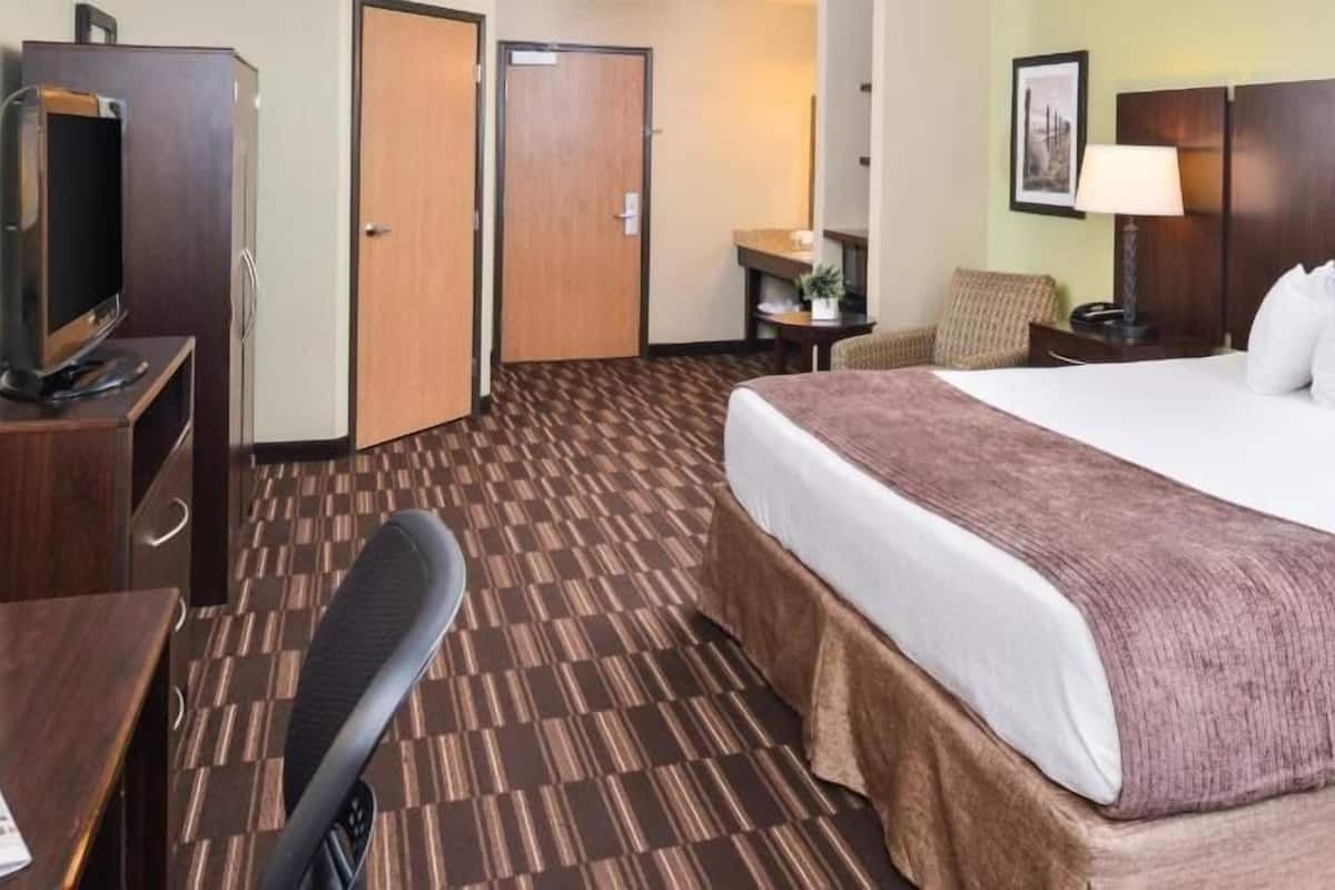 A hotel room with a bed, a desk, a chair, a television, and a door.