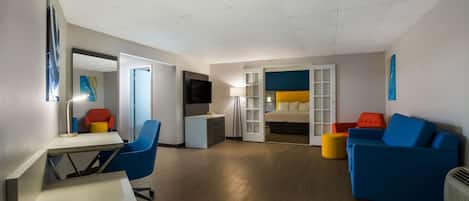 Una sala moderna con un escritorio, sillas azules y naranja, un sofá y una cama con cabecera azul.