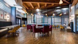 Un comedor amplio con pisos de madera, varias mesas y sillas, e iluminación colgante.
