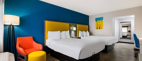 A hotel room with a large bed, a bedside table, a lamp, a chair, and a small ottoman.