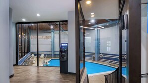 A modern indoor swimming pool area with a glass partition, wooden flooring, and an ATM machine. - Best Western Bordentown Inn (Bordentown)