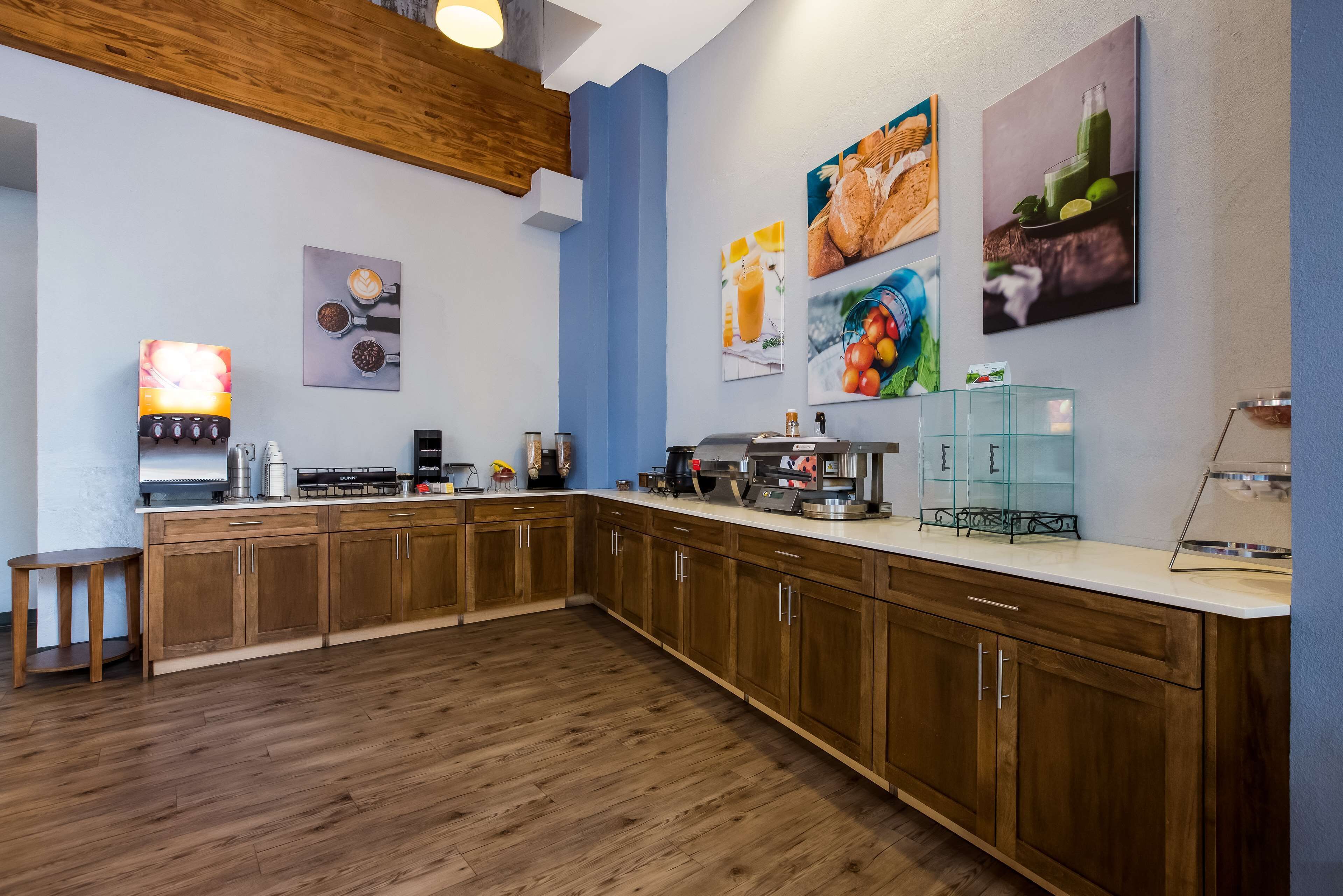 Une cuisine moderne avec des meubles en bois, un plan de travail équipé de divers appareils et des œuvres d’art murales représentant des aliments et des boissons.