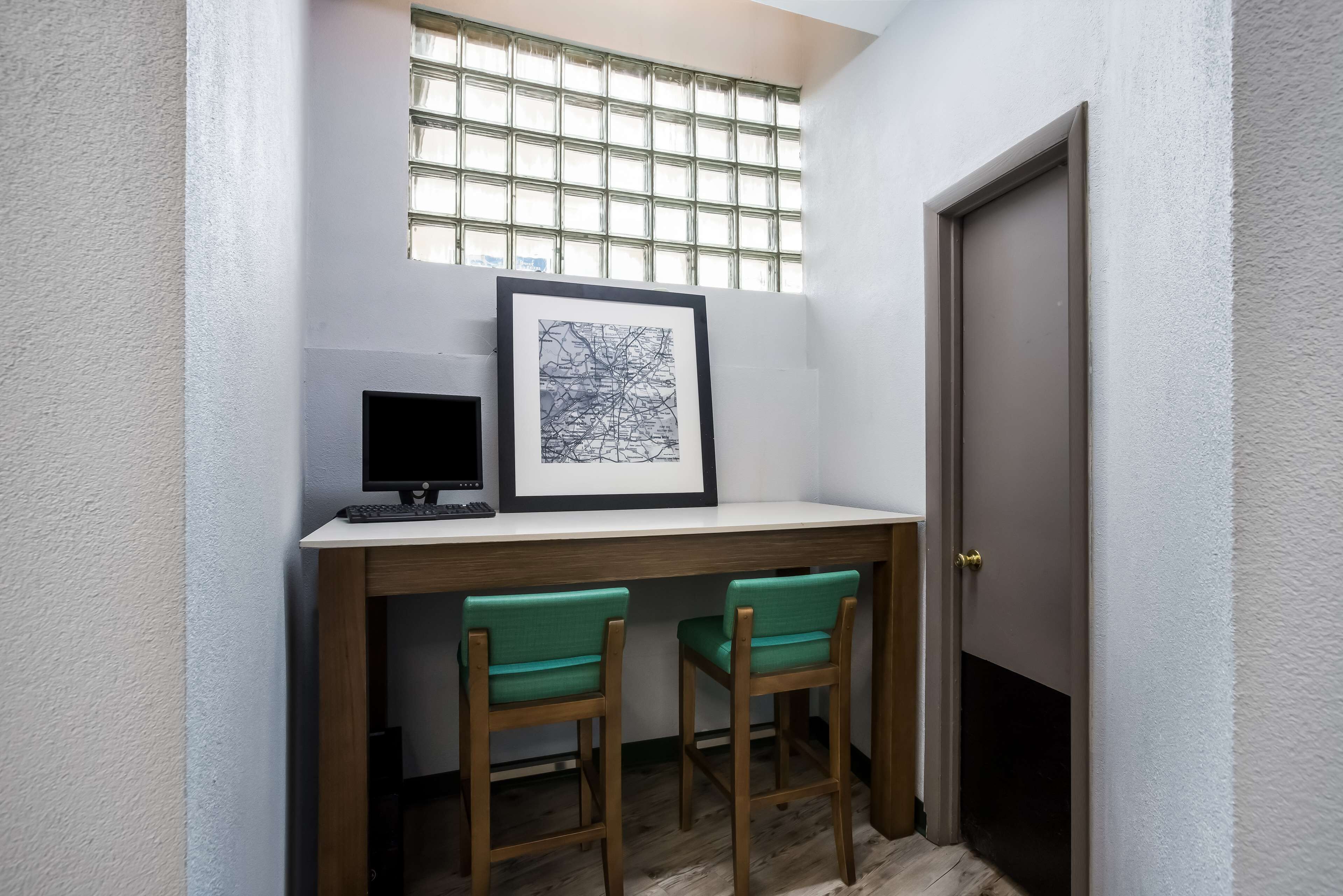 A small office space with a desk, two chairs, a framed picture, and a computer monitor.