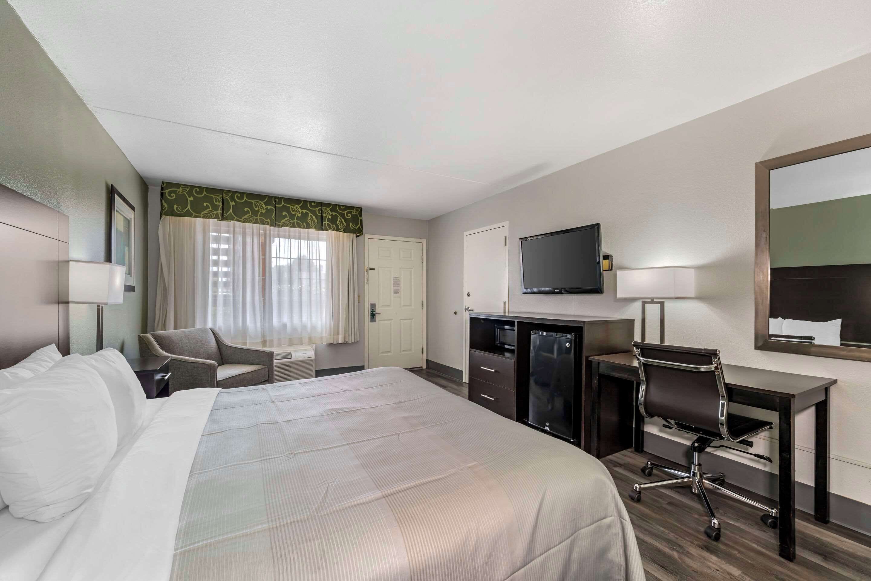 A hotel room with a bed, a desk, a chair, a television, and a minibar.