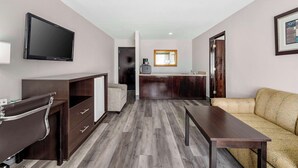 A hotel room with a flat-screen TV mounted on the wall, a wooden desk with drawers, a sofa, and a small kitchenette area with a coffee machine. - Quality Inn Siloam Springs West (Siloam Springs)