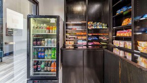 A vending machine stocked with beverages and snacks, a refrigerator with drinks, and shelves with packaged goods. - Quality Inn Siloam Springs West (Siloam Springs)