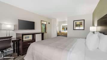 A hotel room with a large bed, a desk with a computer, a microwave, a TV, and a bathroom with a mirror and sink.