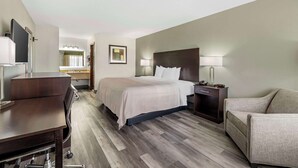 A hotel room with a bed, a desk, a chair, a nightstand, and a lamp. - Quality Inn Siloam Springs West (Siloam Springs)