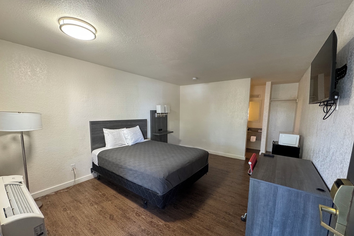 A hotel room with a bed, bedside tables, a desk, a lamp, and a ceiling light.