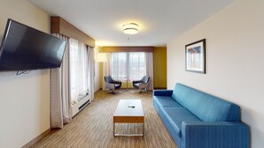 A hotel room with a flat-screen TV, a blue sofa, a small coffee table, and a TV stand. - Holiday Inn Express South Burlington by IHG (South Burlington)
