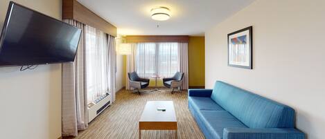 A hotel room with a flat-screen TV, a blue sofa, a small coffee table, and a TV stand.