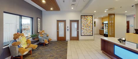 A reception area with a reception desk, two doors, a patterned carpet, and two chairs with teddy bears.