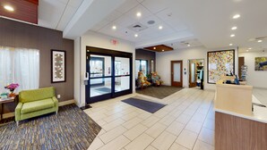 A hotel lobby with a reception desk, a green sofa, a patterned rug, and a large window. - Holiday Inn Express South Burlington by IHG (South Burlington)