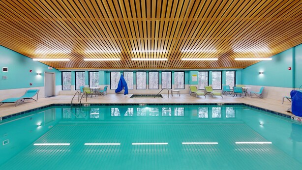 An indoor swimming pool with a wooden ceiling, turquoise walls, and multiple lounge chairs. - Holiday Inn Express South Burlington by IHG (South Burlington)