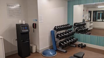 Ein Fitnessstudio mit Wasserspender, Nottelefon, Kurzhanteln und Trainingsgeräten.