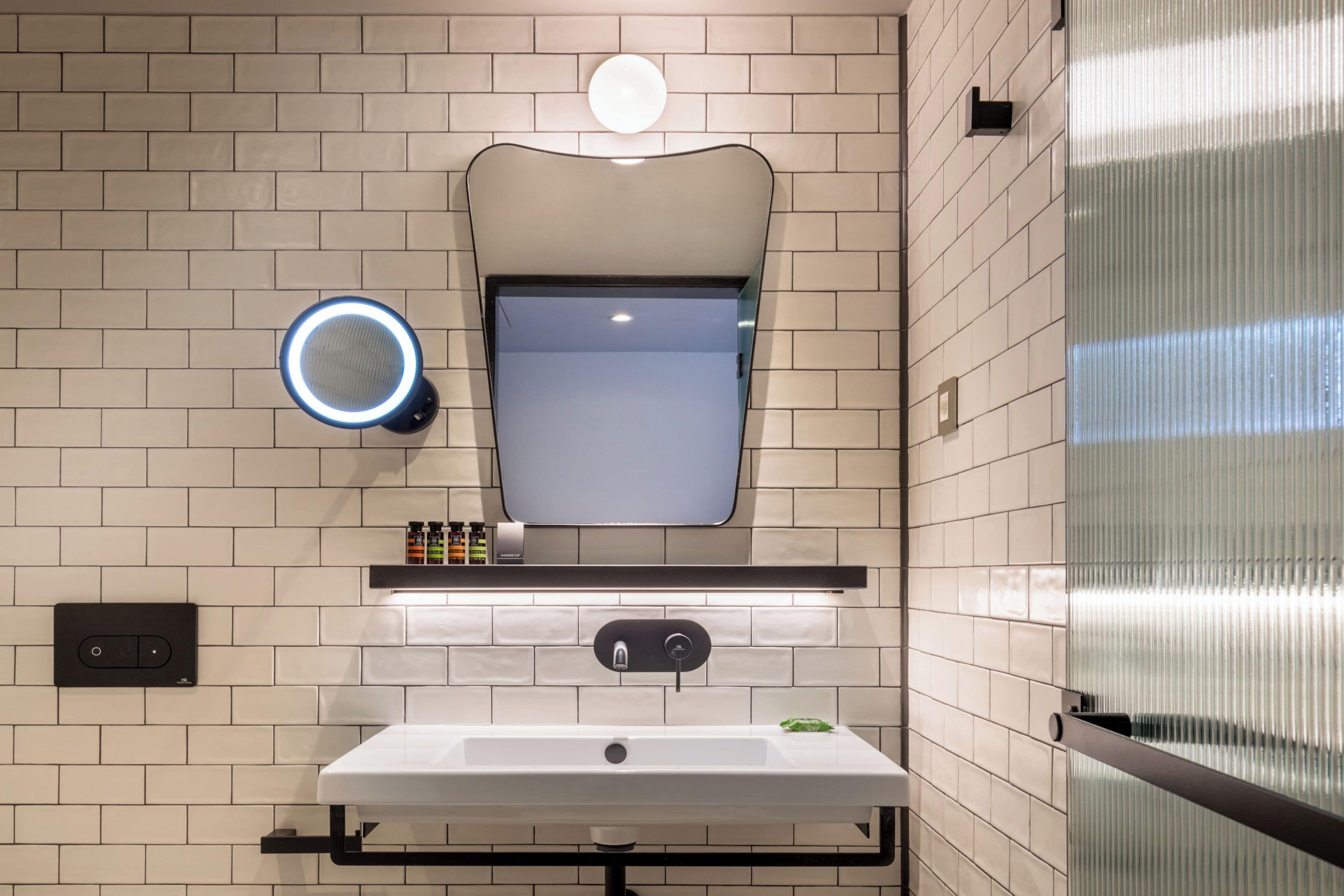 Een moderne badkamer met een wit wastafelmeubel, een spiegel en een ronde lamp boven de spiegel.