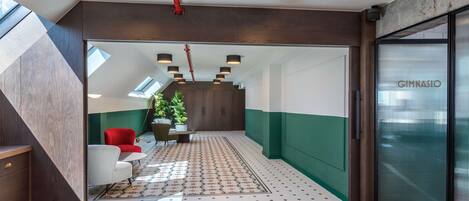 Un interior moderno con una escalera, un área de descanso con una silla roja y un cartel de gimnasio.