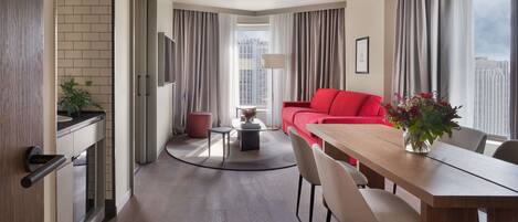 Habitación de hotel moderna con zona de comedor, un sofá rojo y vistas a la ciudad.