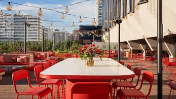 An outdoor dining area with red chairs and tables, a flower vase, and string lights.