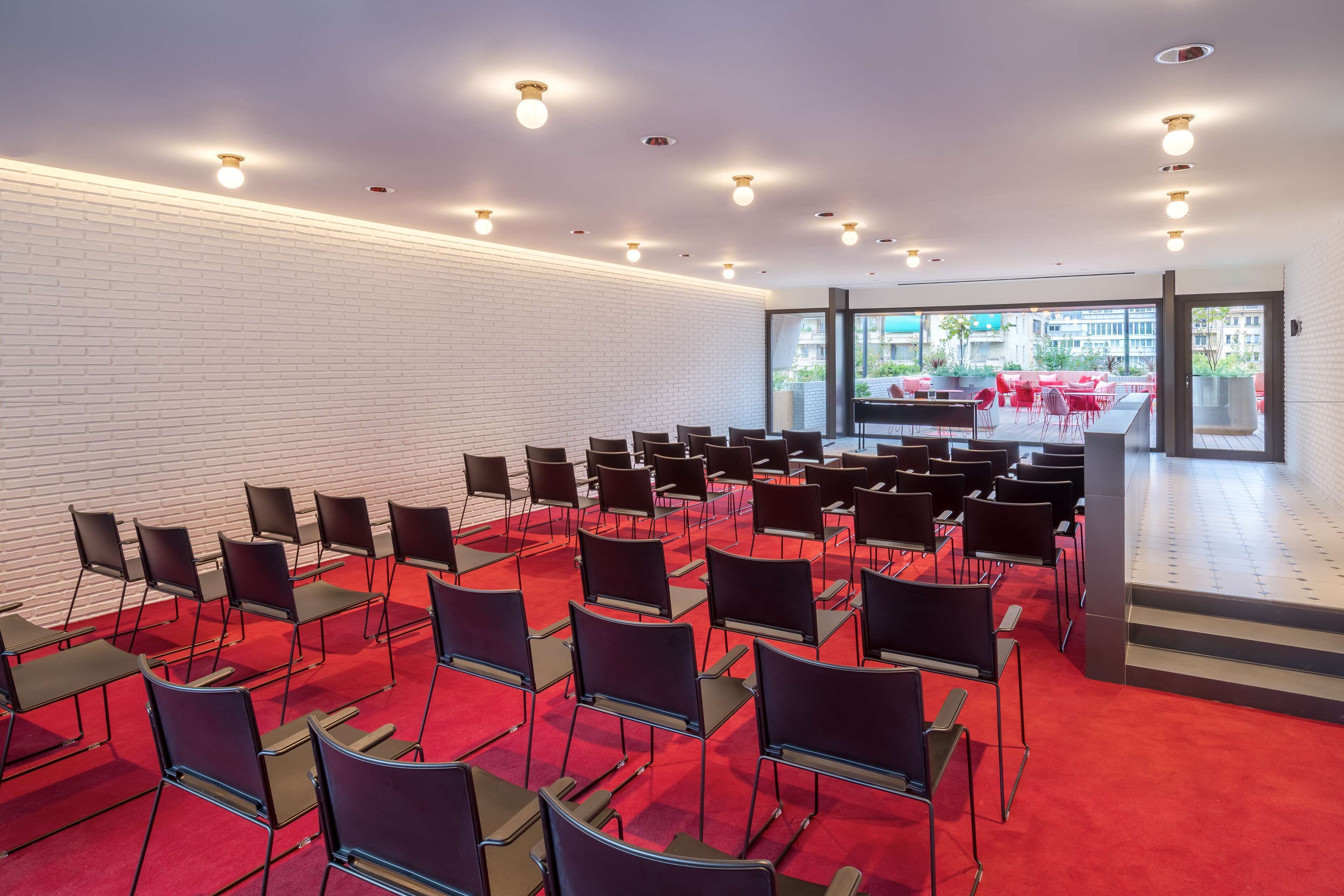 A conference room with rows of chairs, a stage, and a large window offering a view of the city.