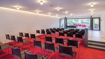 Un salón de conferencias con filas de sillas, un escenario y un amplio ventanal con vistas a la ciudad.