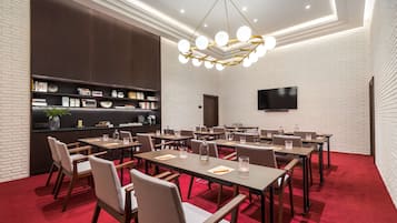 Une salle de conférence équipée de tables, de chaises, d’une bibliothèque, d’un téléviseur et d’un tapis rouge.
