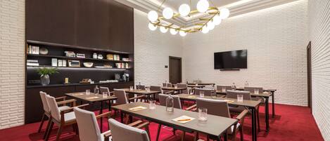A conference room with tables, chairs, a bookshelf, a television, and a red carpet.