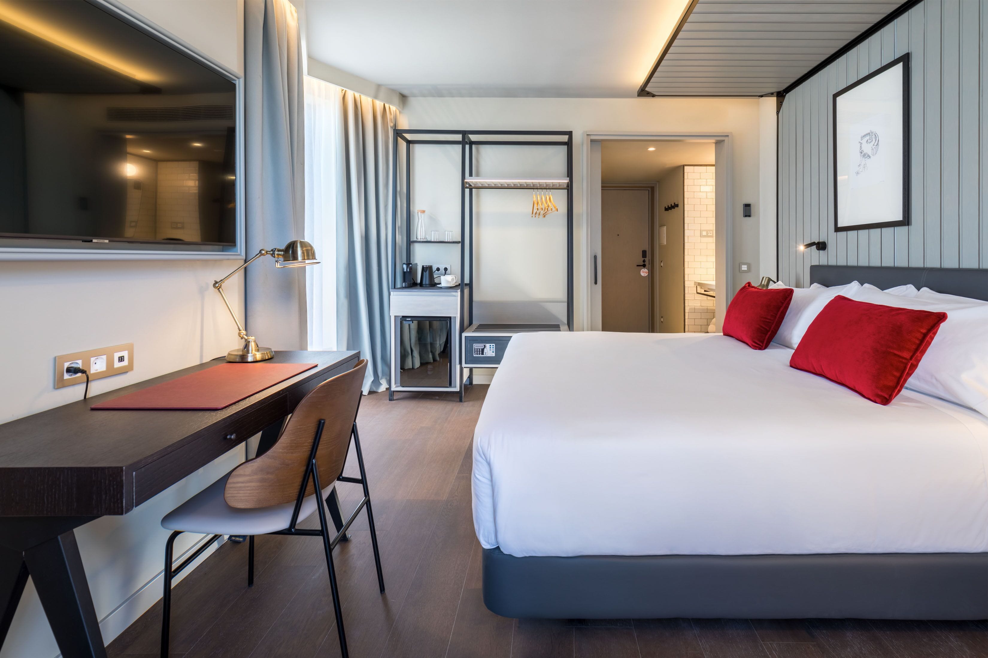 A modern hotel room with a large bed, a desk, and a chair.