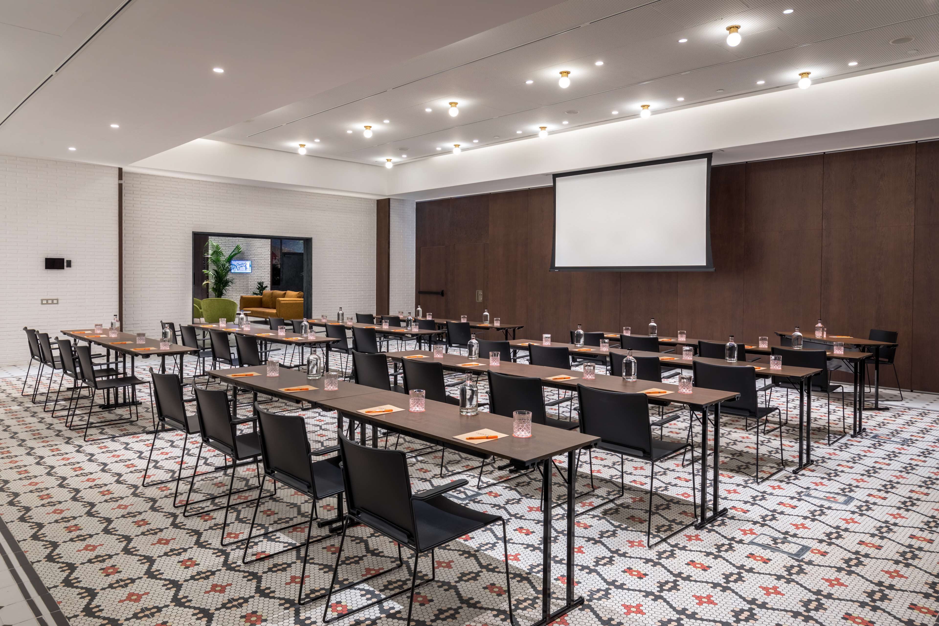 Une salle de conférence équipée de plusieurs tables et chaises, d’un écran de projection et d’un tapis à motifs.
