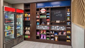 A vending area with a 'Welcome to Commack' sign, a 'Local Honey' chalkboard, and a 'Treats' sign above a shelf with snacks. - Hampton Inn Long Island / Commack (Commack)