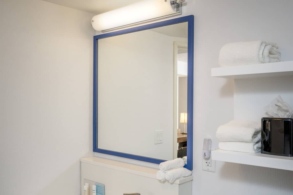 A bathroom with a white sink, a mirror with a blue frame, a toilet, and a shelf with towels.