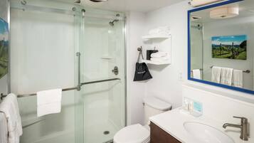 Ein modernes Badezimmer mit einer in Glas abgeschlossenen Dusche, einer weißen Toilette, einem Waschbecken mit Spiegel und einem Handtuchhalter.