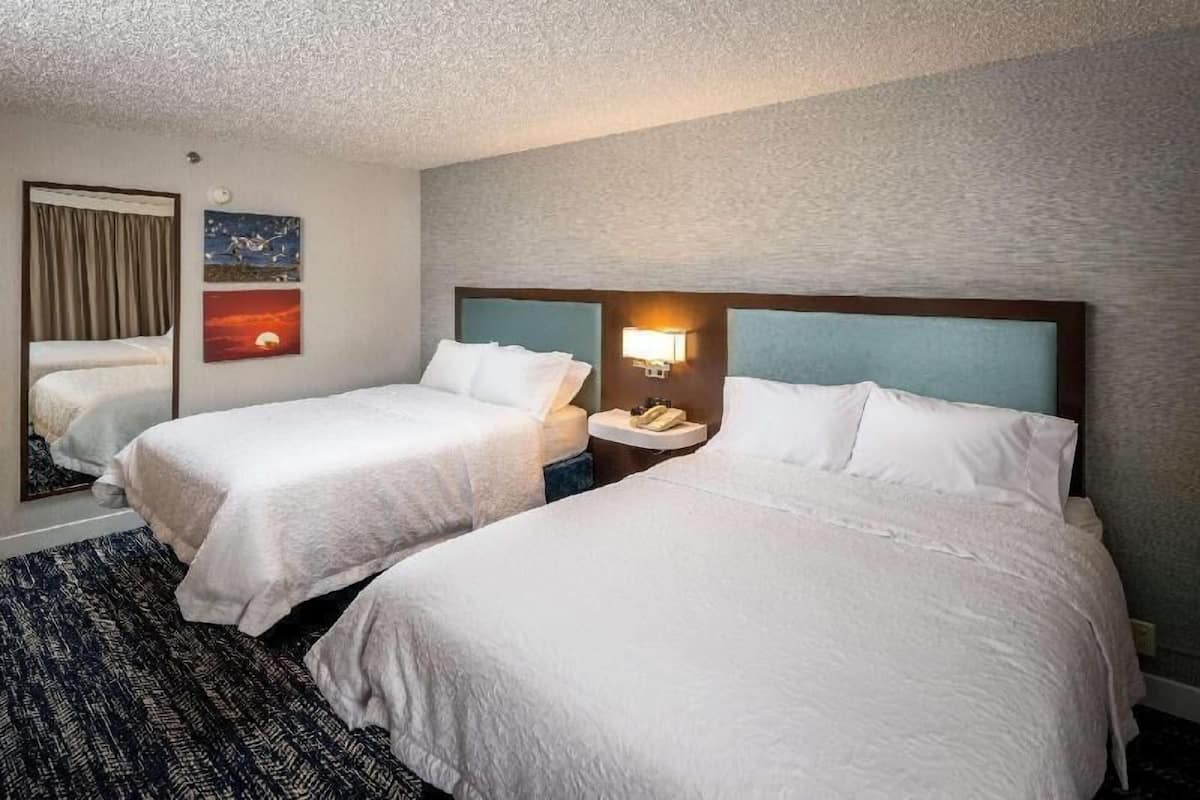 A hotel room with two beds, a nightstand with a lamp, a wall clock, and a framed picture.